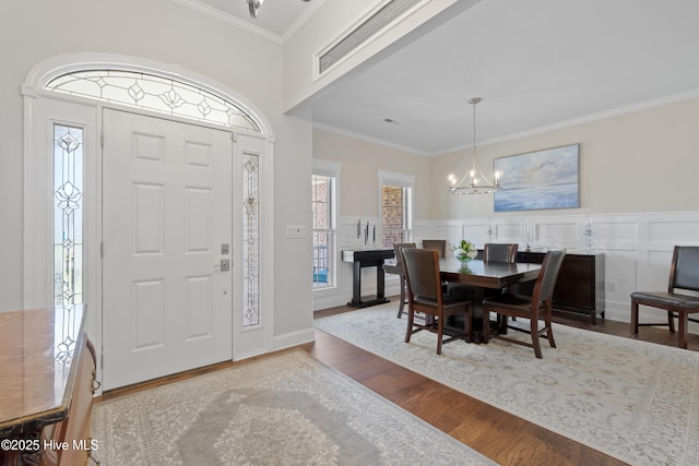 entrance foyer with a wealth of natural light, a notable chandelier, ornamental molding, and wood finished floors