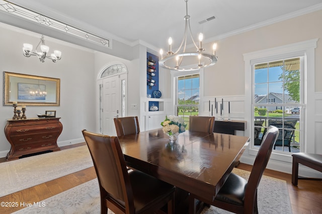 dining space with visible vents, a chandelier, ornamental molding, wood finished floors, and a decorative wall