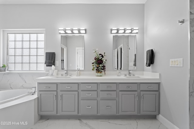 bathroom with a sink, marble finish floor, a garden tub, and double vanity