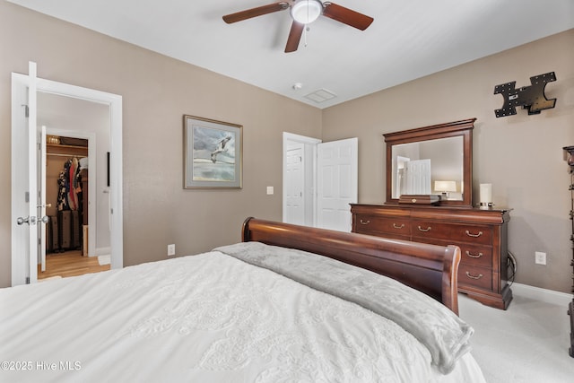 bedroom featuring light carpet, a ceiling fan, a closet, baseboards, and a spacious closet