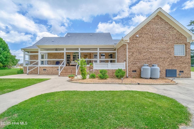 back of property featuring driveway, a yard, covered porch, crawl space, and brick siding