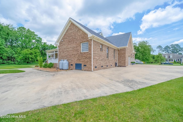 view of side of home featuring brick siding, a shingled roof, a yard, crawl space, and driveway