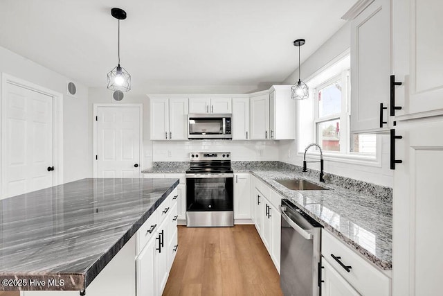 kitchen with a sink, decorative backsplash, stainless steel appliances, white cabinetry, and light wood-type flooring