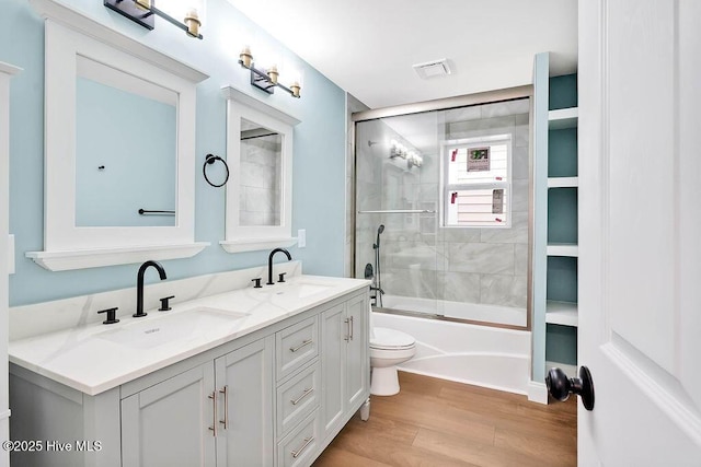 bathroom featuring enclosed tub / shower combo, toilet, wood finished floors, and a sink