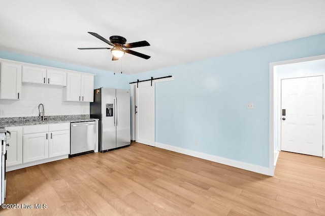 kitchen featuring light stone counters, ceiling fan, a sink, appliances with stainless steel finishes, and a barn door