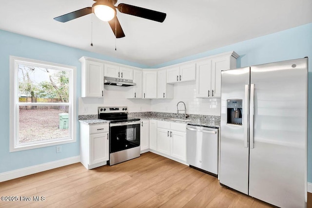 kitchen featuring light stone countertops, light wood-style flooring, a sink, stainless steel appliances, and under cabinet range hood