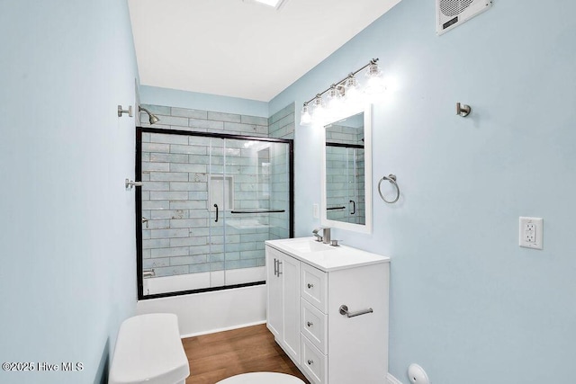 bathroom featuring visible vents, toilet, wood finished floors, shower / bath combination with glass door, and vanity