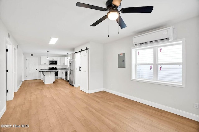 unfurnished living room with a barn door, a wall unit AC, electric panel, light wood-style floors, and a ceiling fan