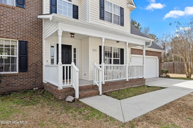 view of exterior entry featuring fence, covered porch, concrete driveway, a garage, and brick siding