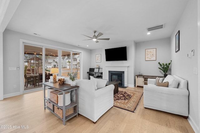 living room featuring visible vents, a ceiling fan, a glass covered fireplace, light wood-style floors, and baseboards