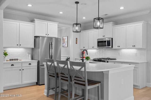 kitchen featuring light wood-type flooring, visible vents, a center island with sink, ornamental molding, and stainless steel appliances