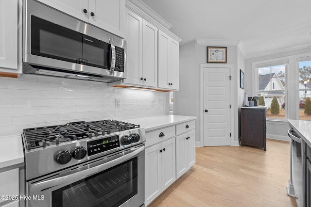 kitchen featuring light wood finished floors, light countertops, white cabinets, appliances with stainless steel finishes, and crown molding