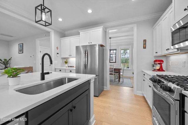 kitchen featuring light countertops, ornamental molding, appliances with stainless steel finishes, white cabinets, and a sink