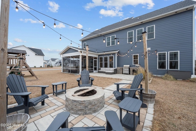 rear view of property with a patio, a playground, an outdoor living space with a fire pit, and a sunroom