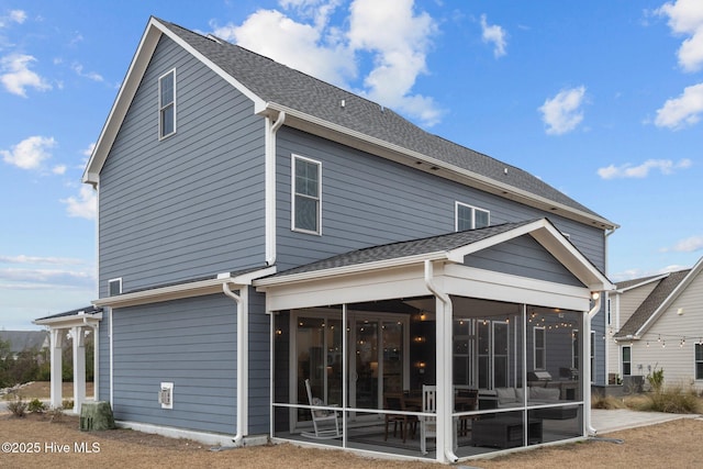 rear view of property featuring a patio, a sunroom, and roof with shingles