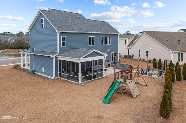 rear view of house featuring a playground, a fire pit, a shingled roof, and a sunroom