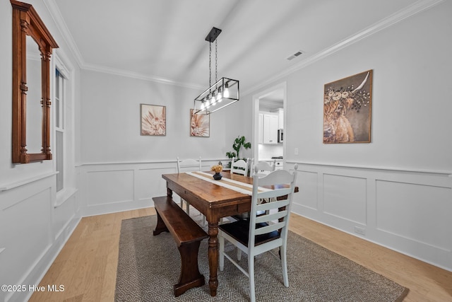 dining room featuring a decorative wall, visible vents, crown molding, and light wood finished floors