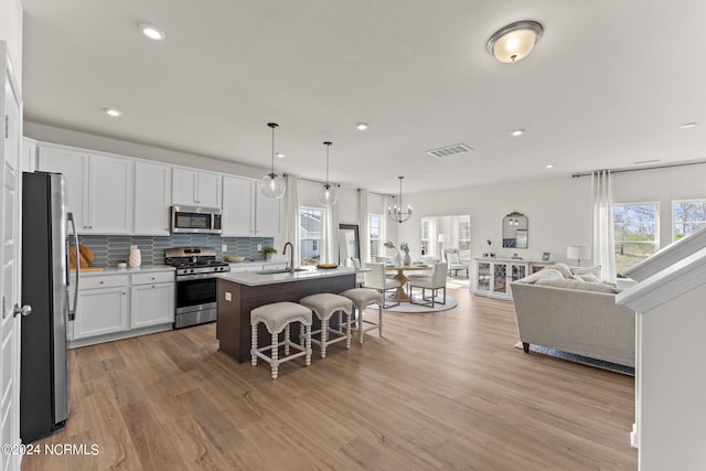 kitchen featuring visible vents, decorative backsplash, appliances with stainless steel finishes, a kitchen breakfast bar, and open floor plan