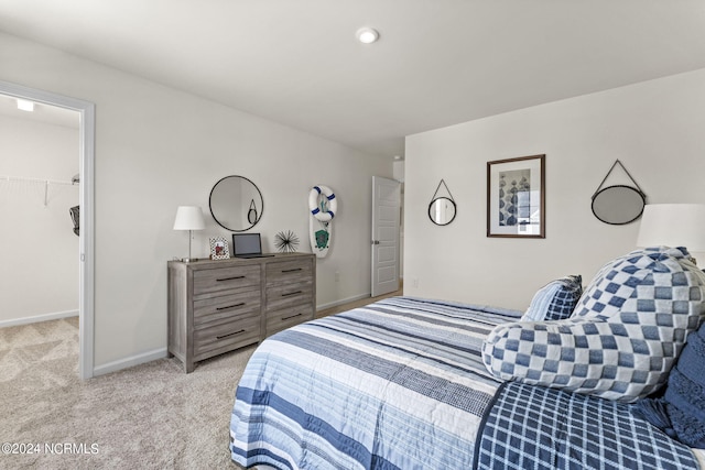 bedroom featuring a walk in closet, baseboards, and light carpet