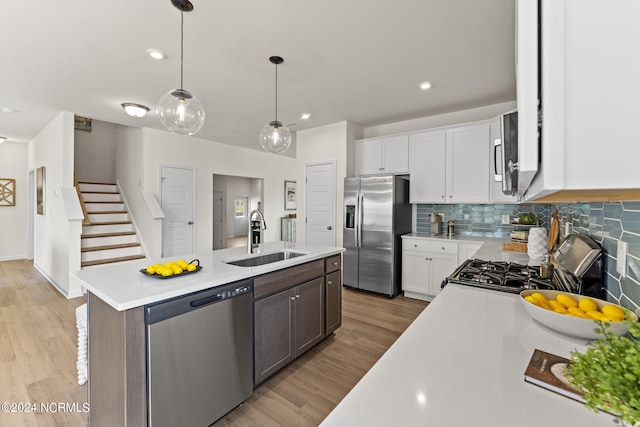 kitchen with a center island with sink, a sink, light countertops, appliances with stainless steel finishes, and white cabinetry