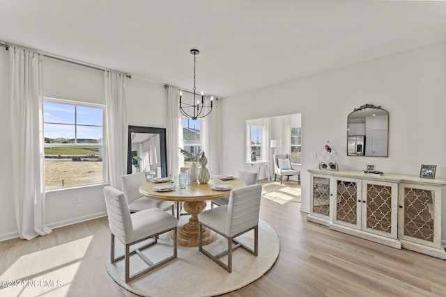 dining space with light wood-style flooring, a notable chandelier, a healthy amount of sunlight, and baseboards