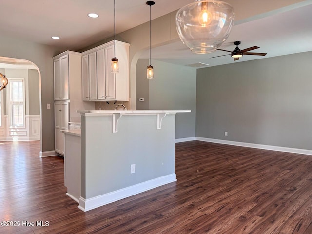 kitchen featuring a breakfast bar area, dark wood finished floors, arched walkways, light countertops, and white cabinetry