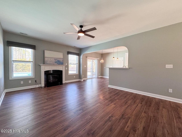 unfurnished living room featuring a ceiling fan, baseboards, visible vents, dark wood-type flooring, and a glass covered fireplace