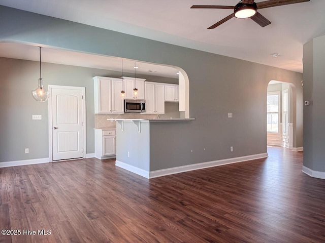 kitchen with stainless steel microwave, a breakfast bar area, dark wood-style floors, arched walkways, and white cabinets