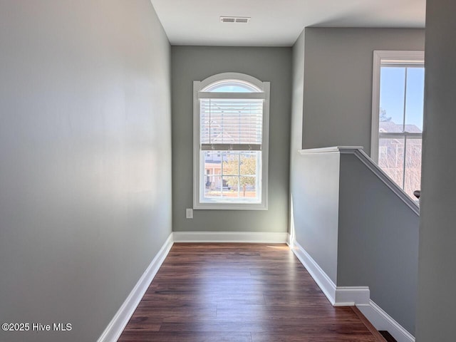 empty room with dark wood finished floors, visible vents, and baseboards