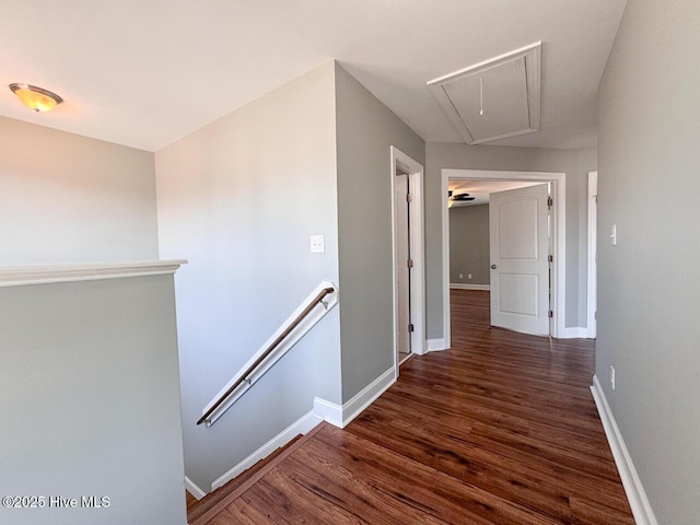 hall featuring an upstairs landing, attic access, baseboards, and wood finished floors