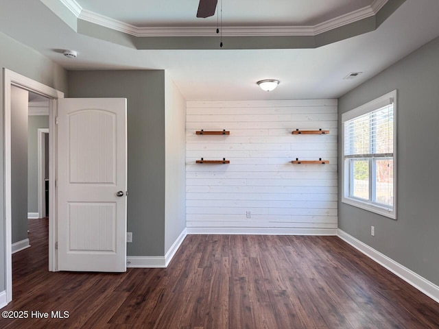 empty room with visible vents, baseboards, dark wood finished floors, a tray ceiling, and ornamental molding