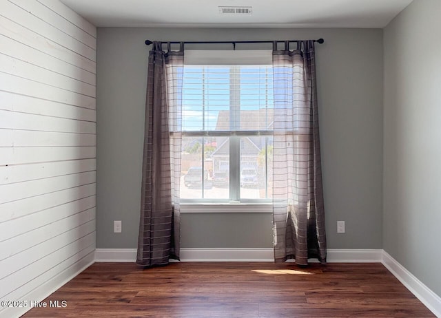 empty room featuring visible vents, baseboards, wood finished floors, and wood walls