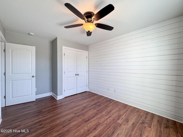 unfurnished bedroom featuring a closet, baseboards, dark wood finished floors, and a ceiling fan