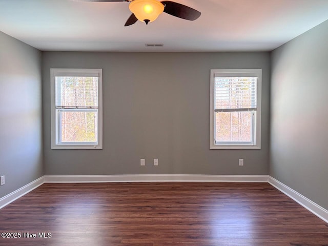 empty room with a wealth of natural light, dark wood-style floors, a ceiling fan, and baseboards