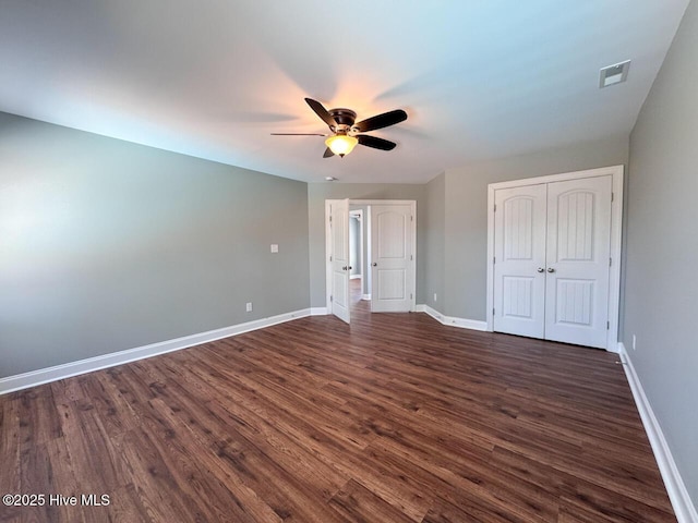 unfurnished bedroom featuring dark wood-style floors, baseboards, visible vents, ceiling fan, and a closet