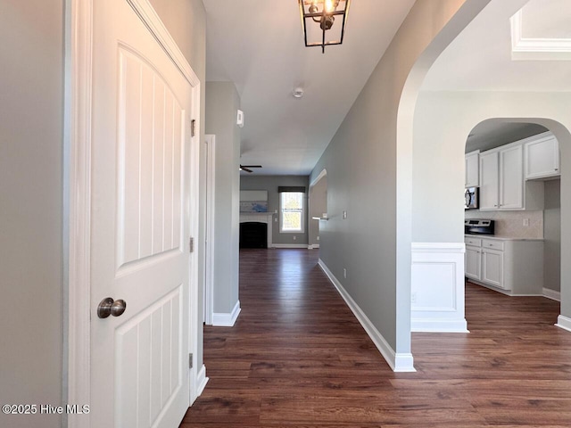 corridor featuring dark wood-style floors, baseboards, and arched walkways