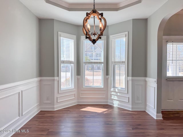 unfurnished dining area featuring a raised ceiling, an inviting chandelier, and dark wood-style floors