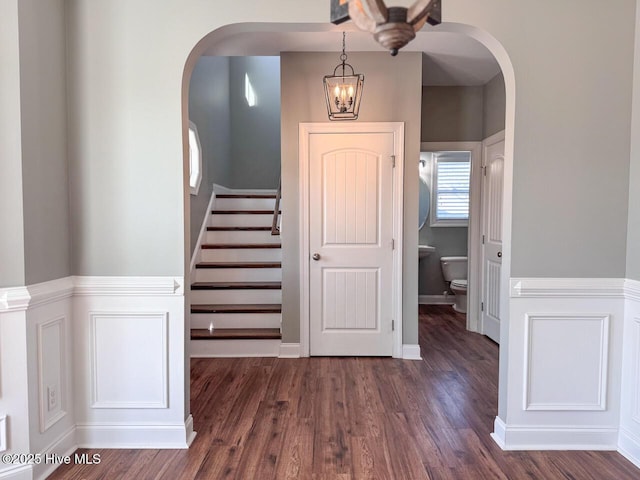 stairs with arched walkways, a decorative wall, and wood finished floors