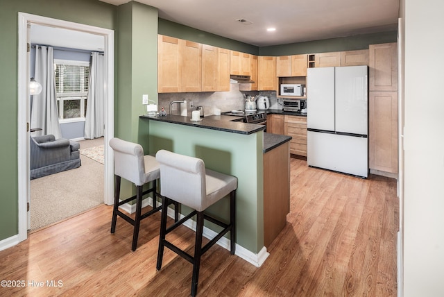 kitchen featuring dark countertops, light brown cabinets, decorative backsplash, light wood-style floors, and white appliances