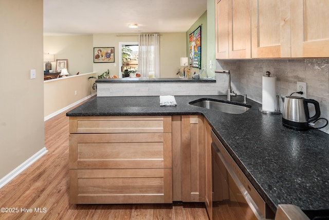 kitchen featuring a peninsula, light wood-style flooring, backsplash, and a sink