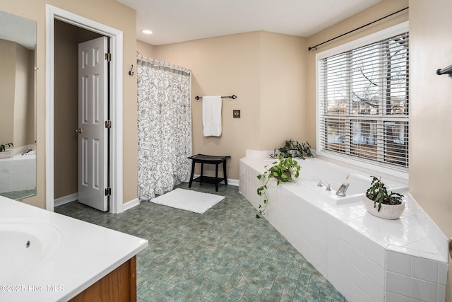 full bathroom featuring baseboards, a garden tub, and vanity