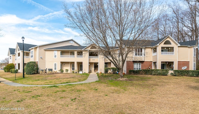 multi unit property featuring brick siding, a balcony, and a front yard