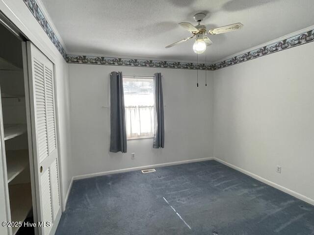 spare room featuring ceiling fan, crown molding, baseboards, and dark colored carpet