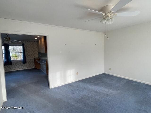 empty room featuring a ceiling fan, dark colored carpet, and baseboards