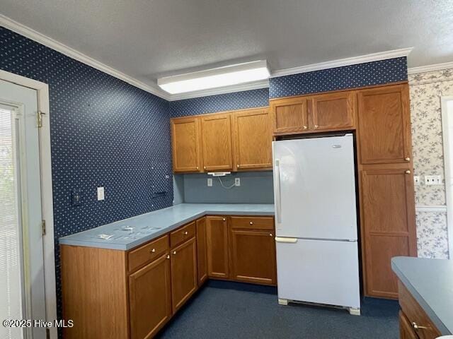 kitchen with wallpapered walls, light countertops, ornamental molding, brown cabinets, and freestanding refrigerator