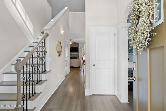 corridor with ornamental molding, wood finished floors, baseboards, a towering ceiling, and stairs