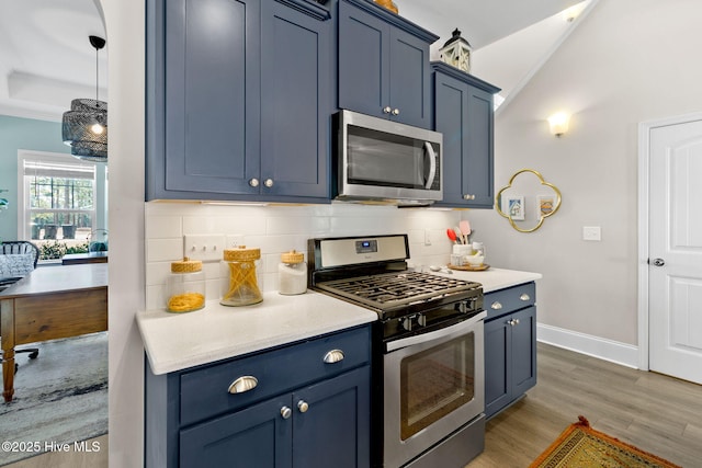 kitchen with blue cabinets, wood finished floors, appliances with stainless steel finishes, light countertops, and decorative backsplash