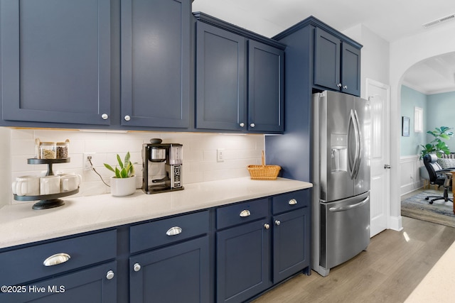 kitchen featuring visible vents, blue cabinetry, light wood-style floors, arched walkways, and stainless steel fridge