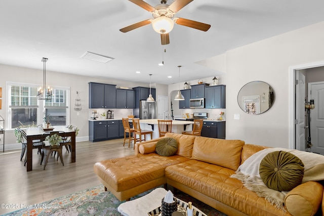 living room with visible vents, light wood finished floors, baseboards, recessed lighting, and ceiling fan with notable chandelier