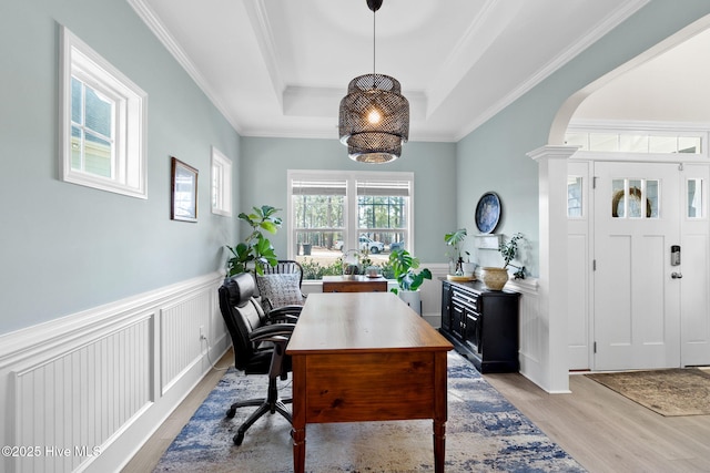 home office featuring light wood finished floors, arched walkways, crown molding, wainscoting, and a raised ceiling